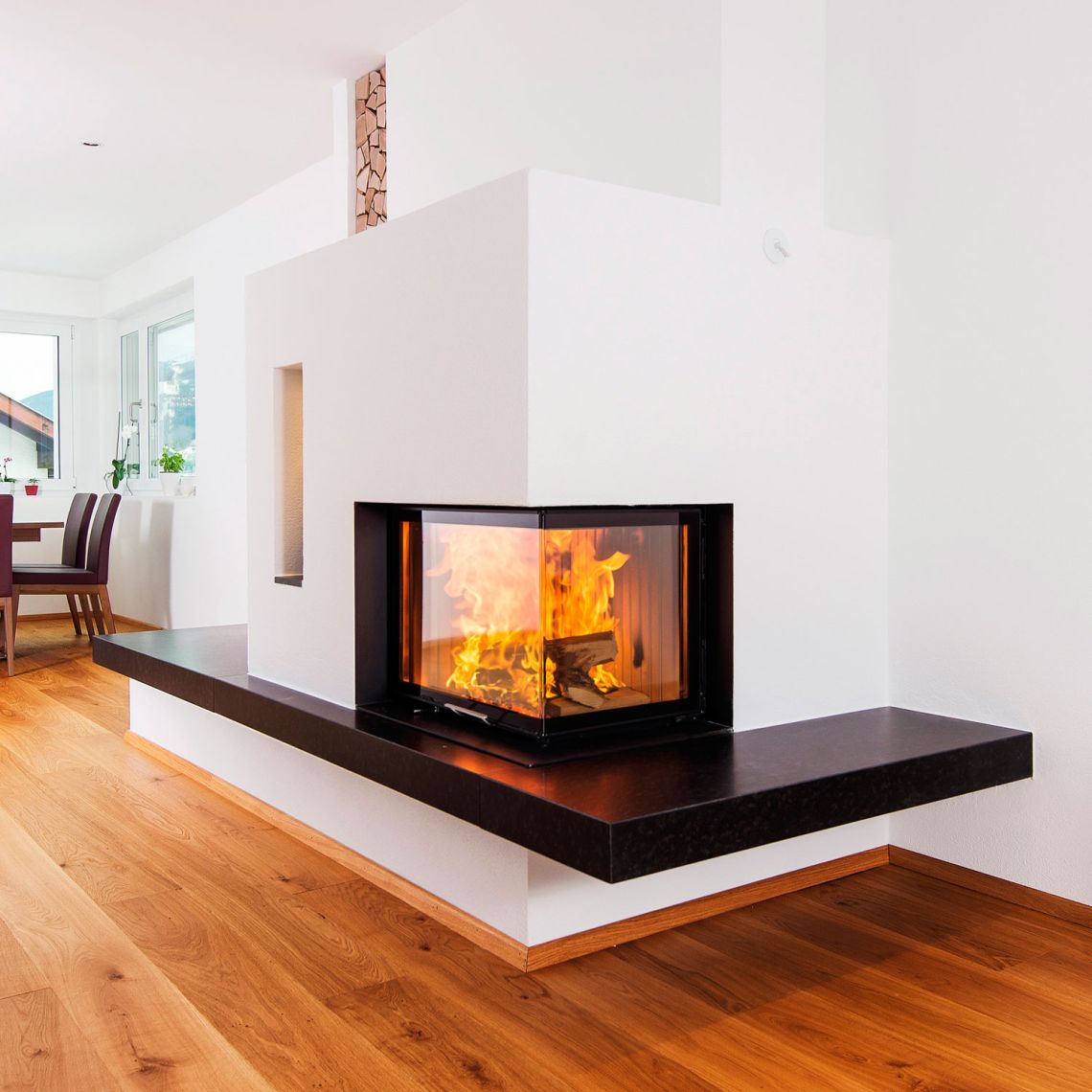 Eck-Cheminée mit hochschiebbarer Glasscheibe, verputzter Verkleidung und Cheminéebank.