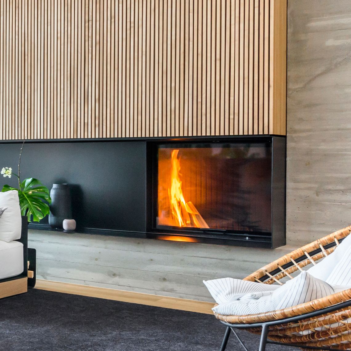 In Wohnwand integriertes Cheminée mit hochschiebbarer Glasscheibe. Bank in Beton, Verkleidung in Holz.