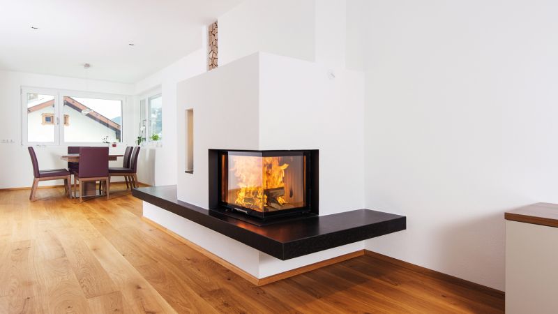 Cheminée mit hochschiebbarer Glasscheibe 2-seitig, mit schwarzer Cheminéebank, weiss verputzt.